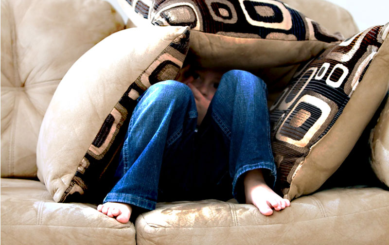 young girl hiding under pillow on a sofaafraid