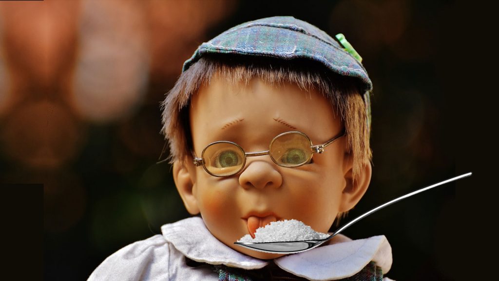 Male preschooler with glasses and a hat sticking out tongue to taste sugar on a spoon